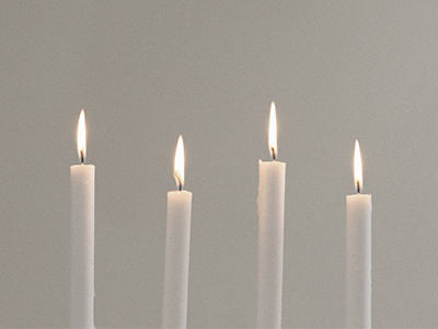 Four lit thin candles against a gray background.