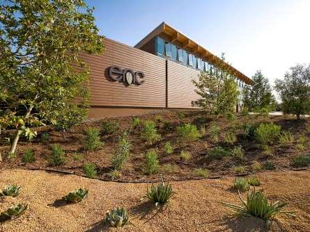 A building with "enc" written on the side. Landscaping with sparse desertous plants is in front. The sun shines.