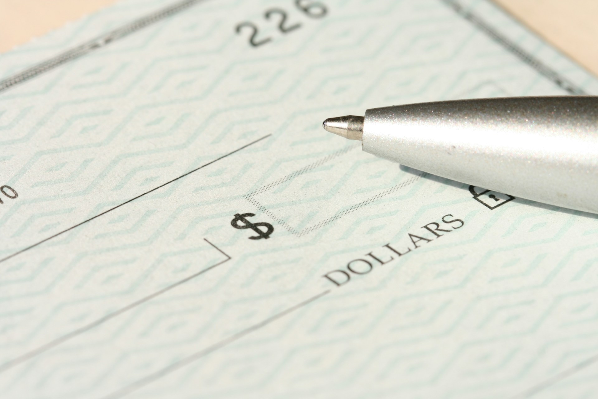 The tip of a ballpoint pen sits atop a blank check.